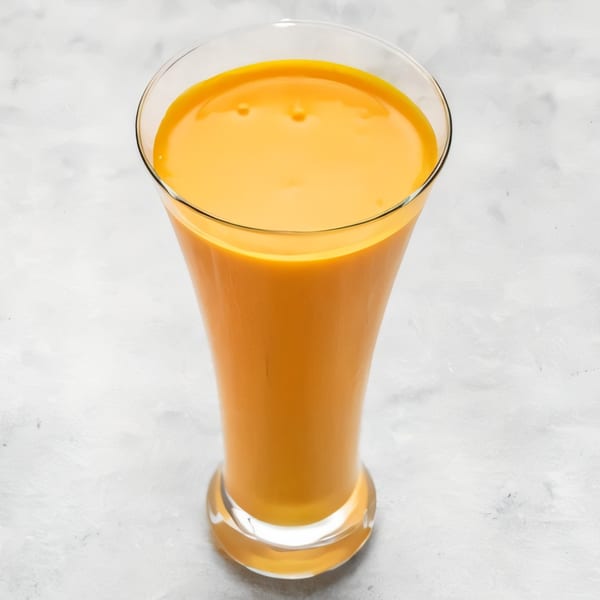 A tall glass of vibrant orange mango lassi, a traditional Indian drink, on a light background.